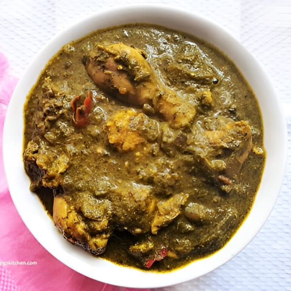 A white bowl filled with green Indian chicken curry, garnished with red chilies.