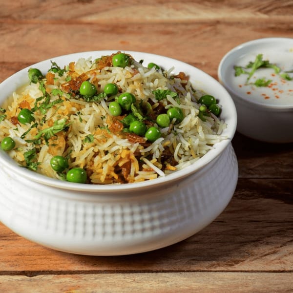 Peas Pulao, an Indian rice dish with green peas and herbs, served with raita.