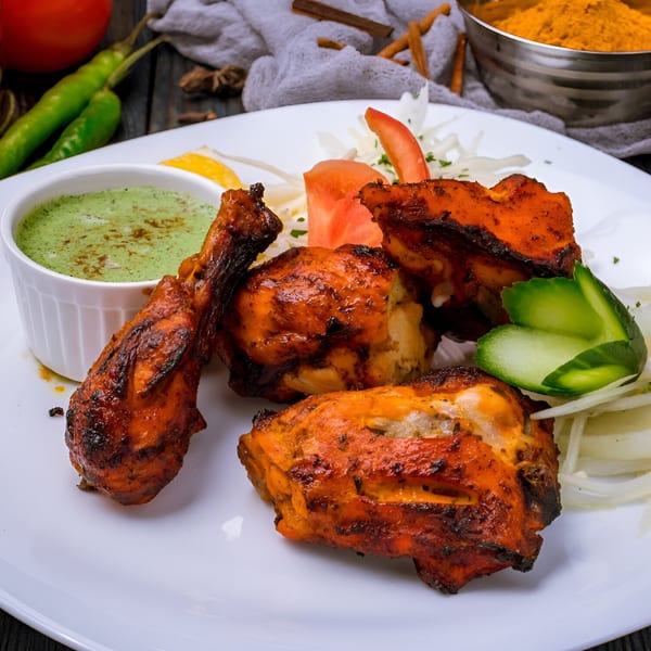 Spice Fine Indian Cuisine's Tandoori Chicken with green chutney, sliced onions, tomato, and cucumber.