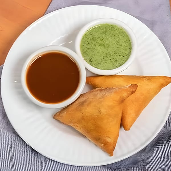 Two golden-brown samosas with green and brown chutneys on a white plate at Spice Fine Indian Cuisine.