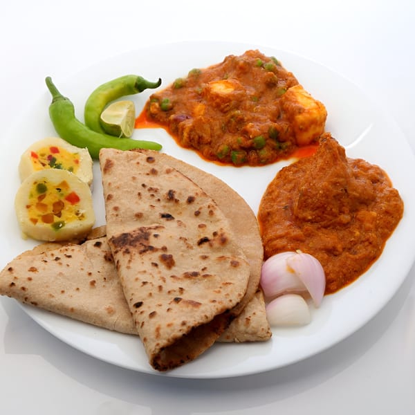 Indian thali with roti, paneer curry, vegetable curry, green chilies, and sliced onions.