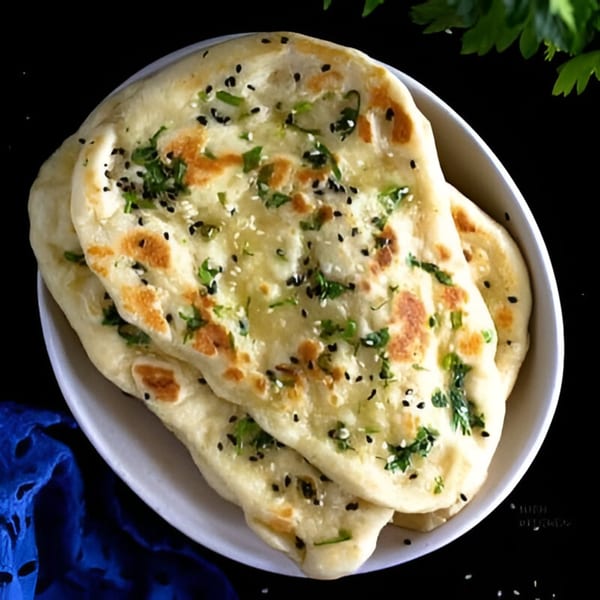 Freshly baked Indian naan bread, garnished with cilantro and sesame seeds, in a white bowl.