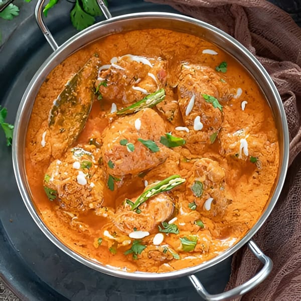 A close-up of Indian butter chicken curry in a metal bowl, garnished with green chilies and cream.