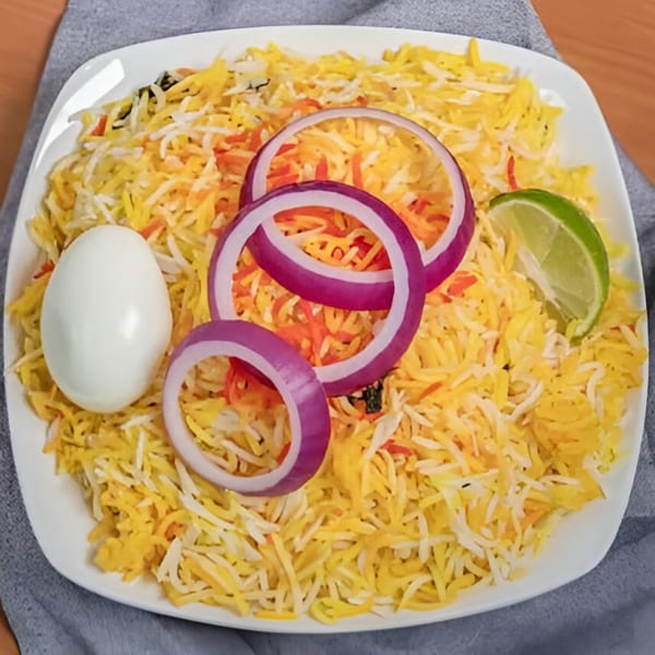Indian biryani with yellow rice, red onion rings, a hard-boiled egg, and a lime wedge.