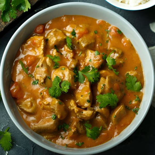 A bowl of Indian chicken curry with a rich orange sauce and fresh cilantro garnish.
